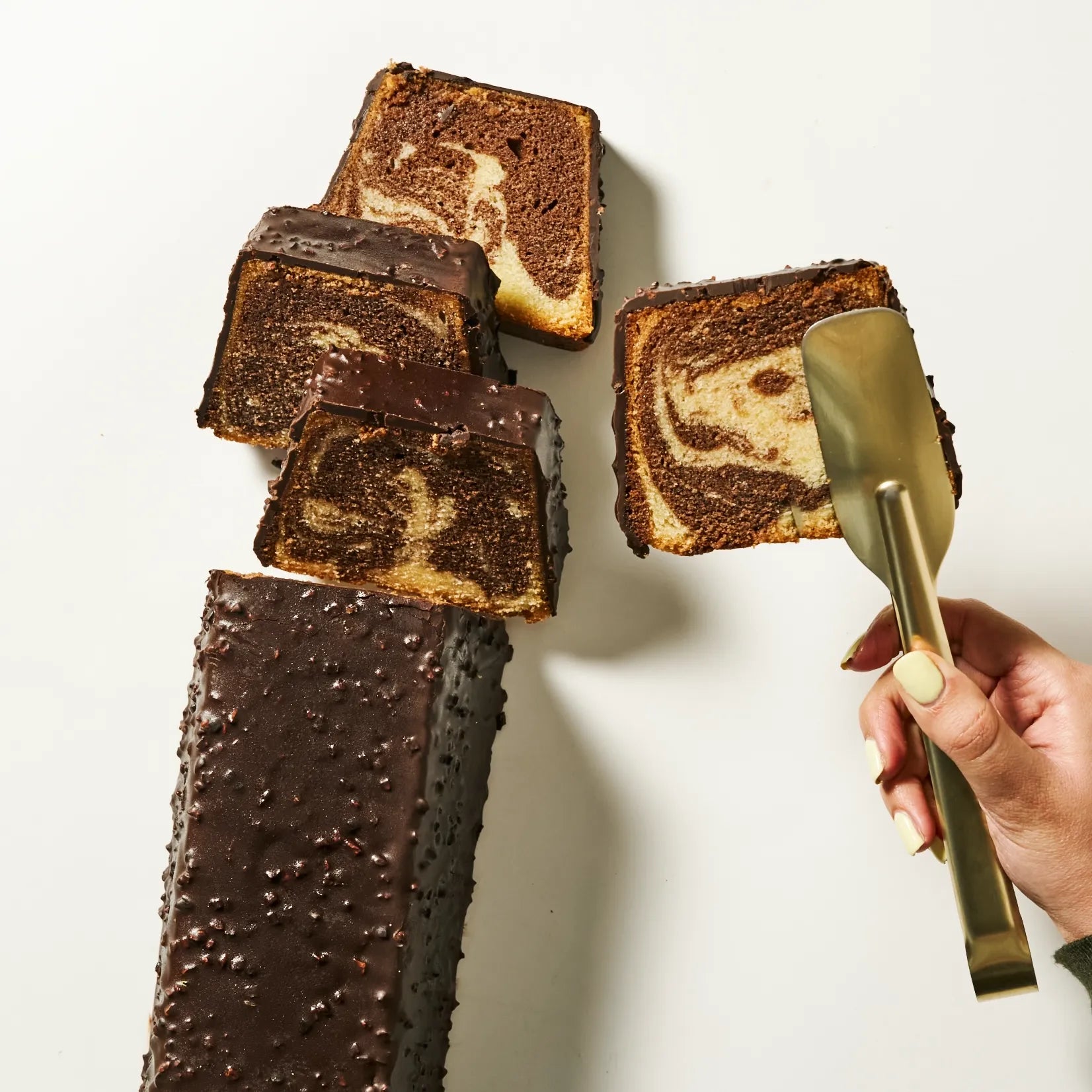 Vue du dessus du cake marbré entier glacé au chocolat noir amande avec une part servie à la pince.