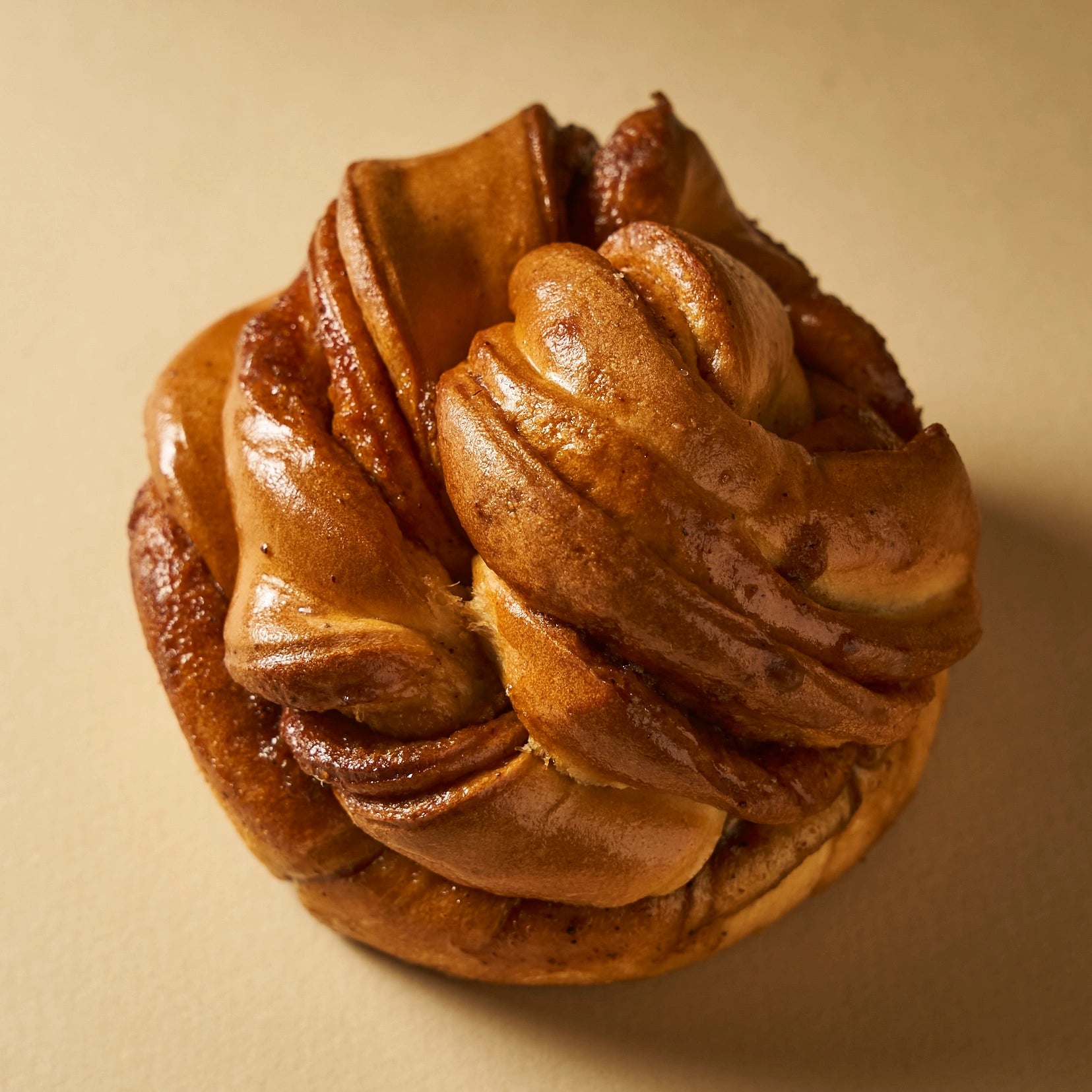 Cinnamon roll artisanal doré et brillant façonné en tressage par le Chef Jeffrey Cagnes sur fond beige.