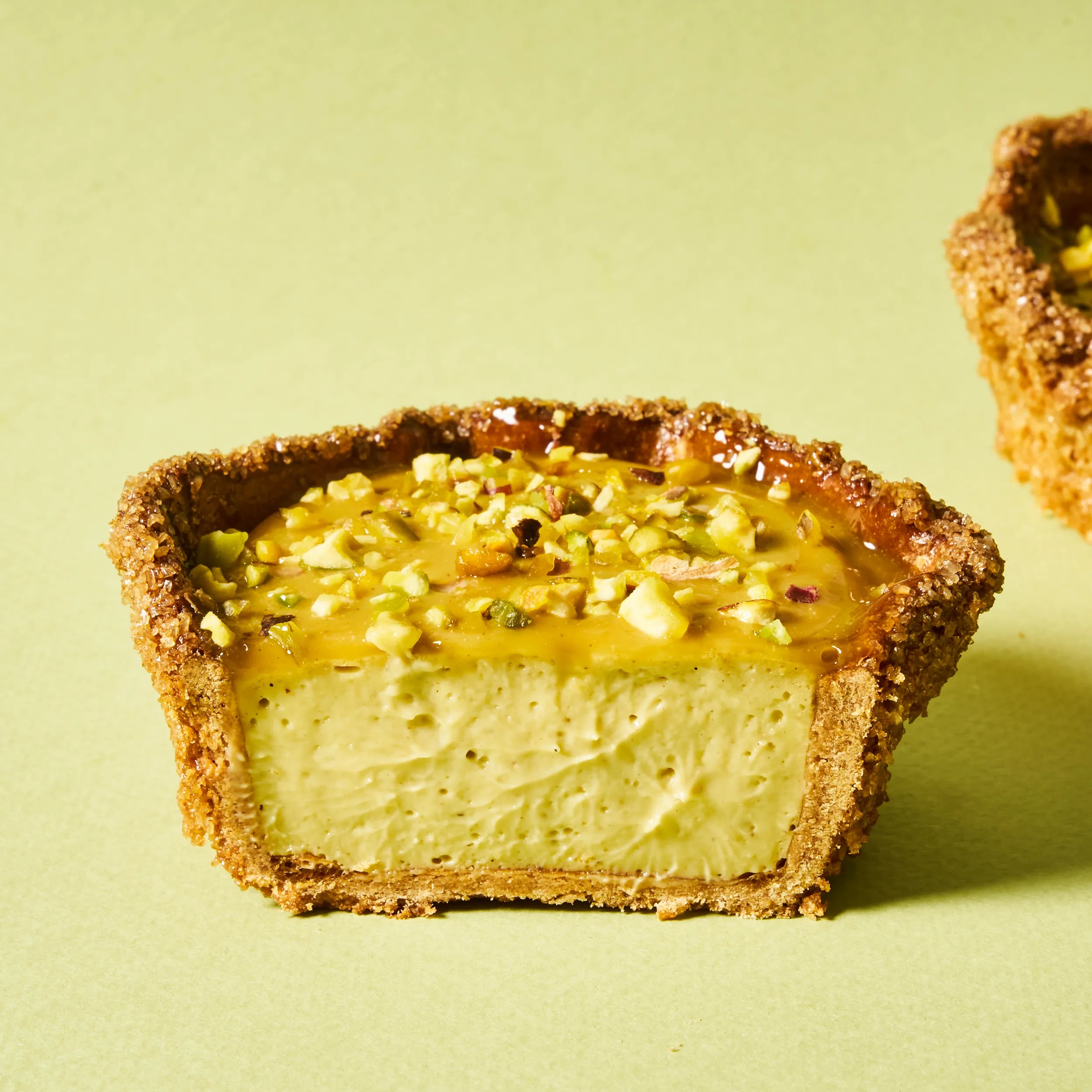 Coupe nette d'un flan pistache individuel de Jeffrey Cagnes, révélant la texture dense et fondante du crémeux ainsi que l'épaisseur de sa pâte sucrée dorée.