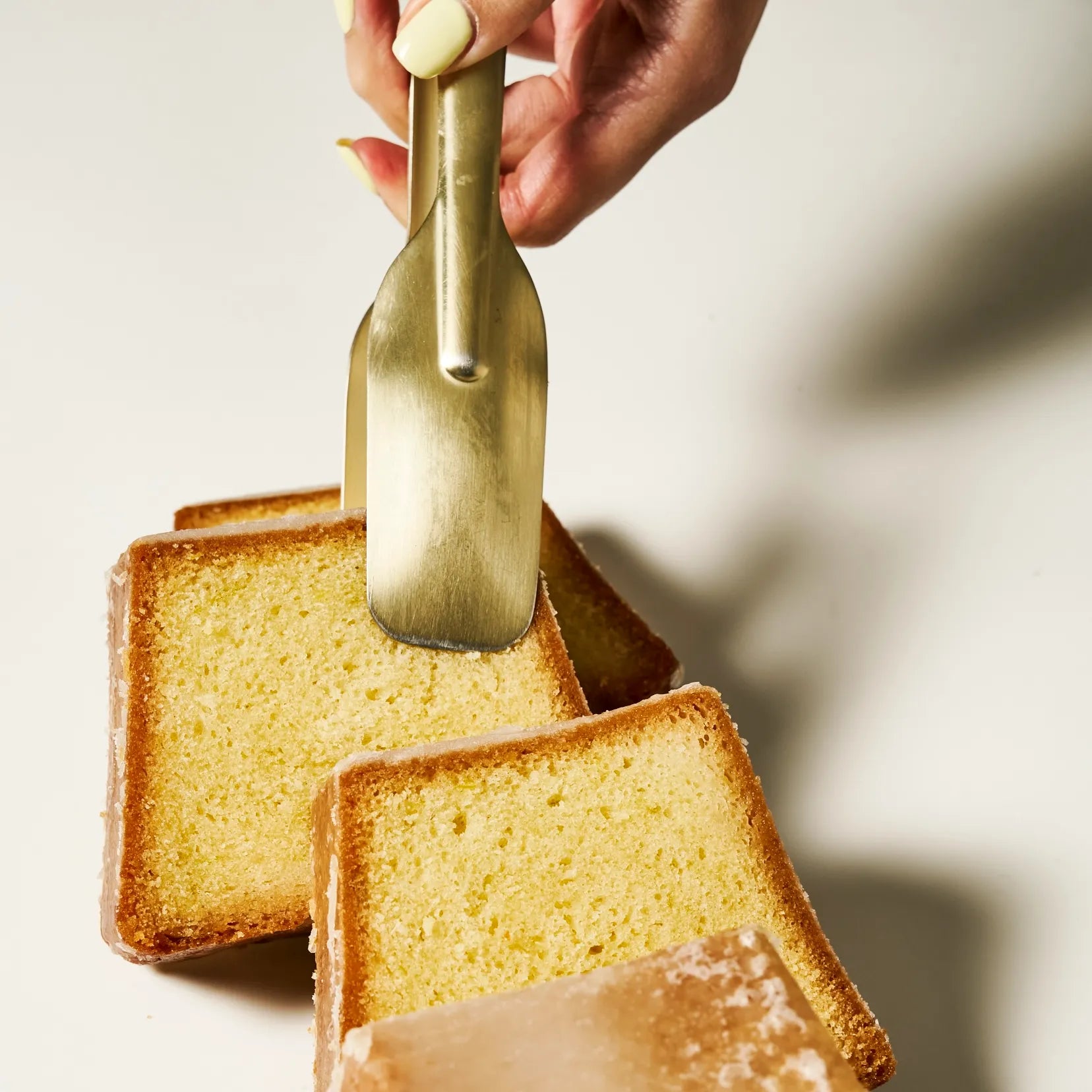 Pince à servir en laiton saisissant une part de cake au citron vert fondant de la Maison Jeffrey Cagnes.