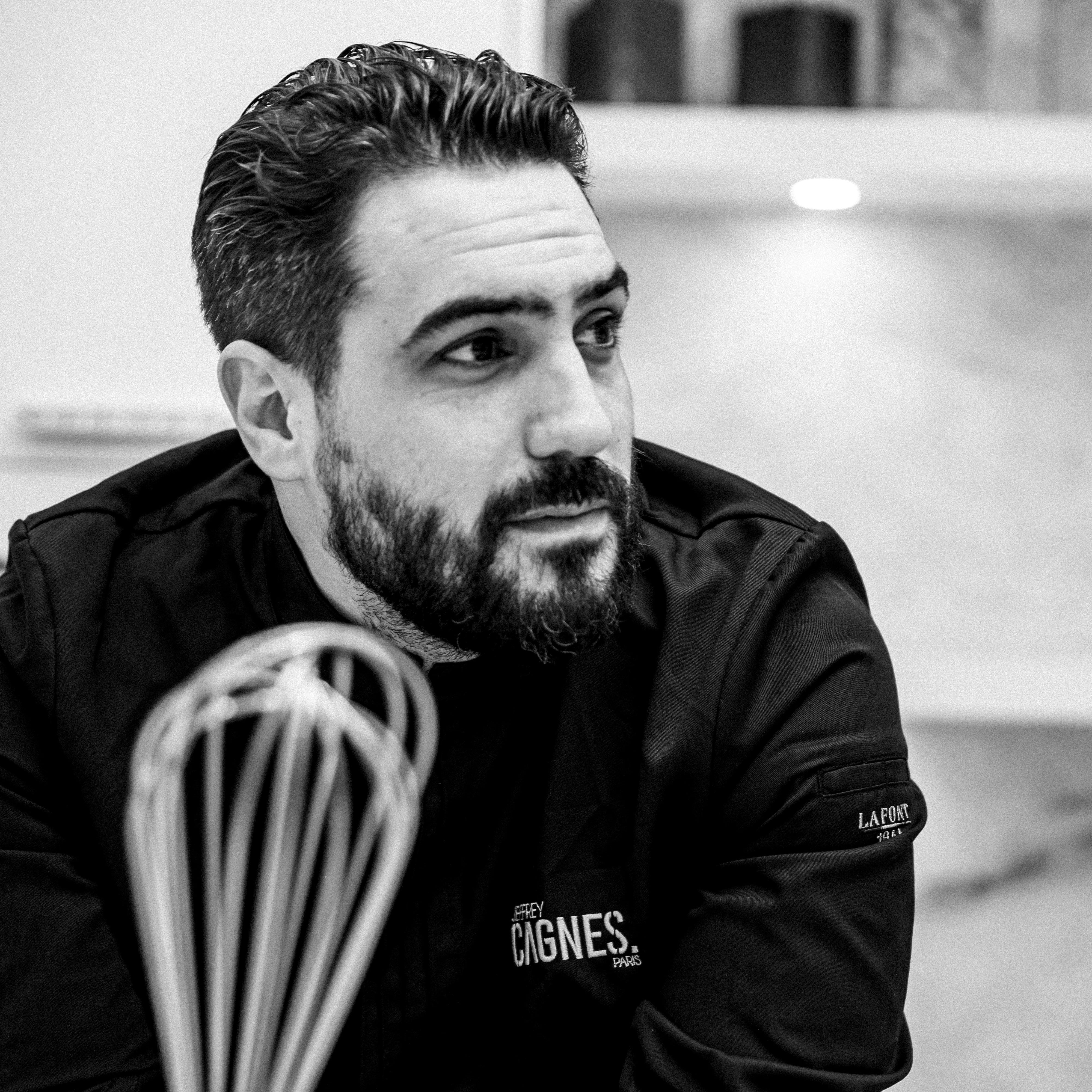 Portrait à la taille du Chef Jeffrey Cagnes en veste de cuisine noire, debout dans son laboratoire avec le logo Jeffrey Cagnes Paris brodé.