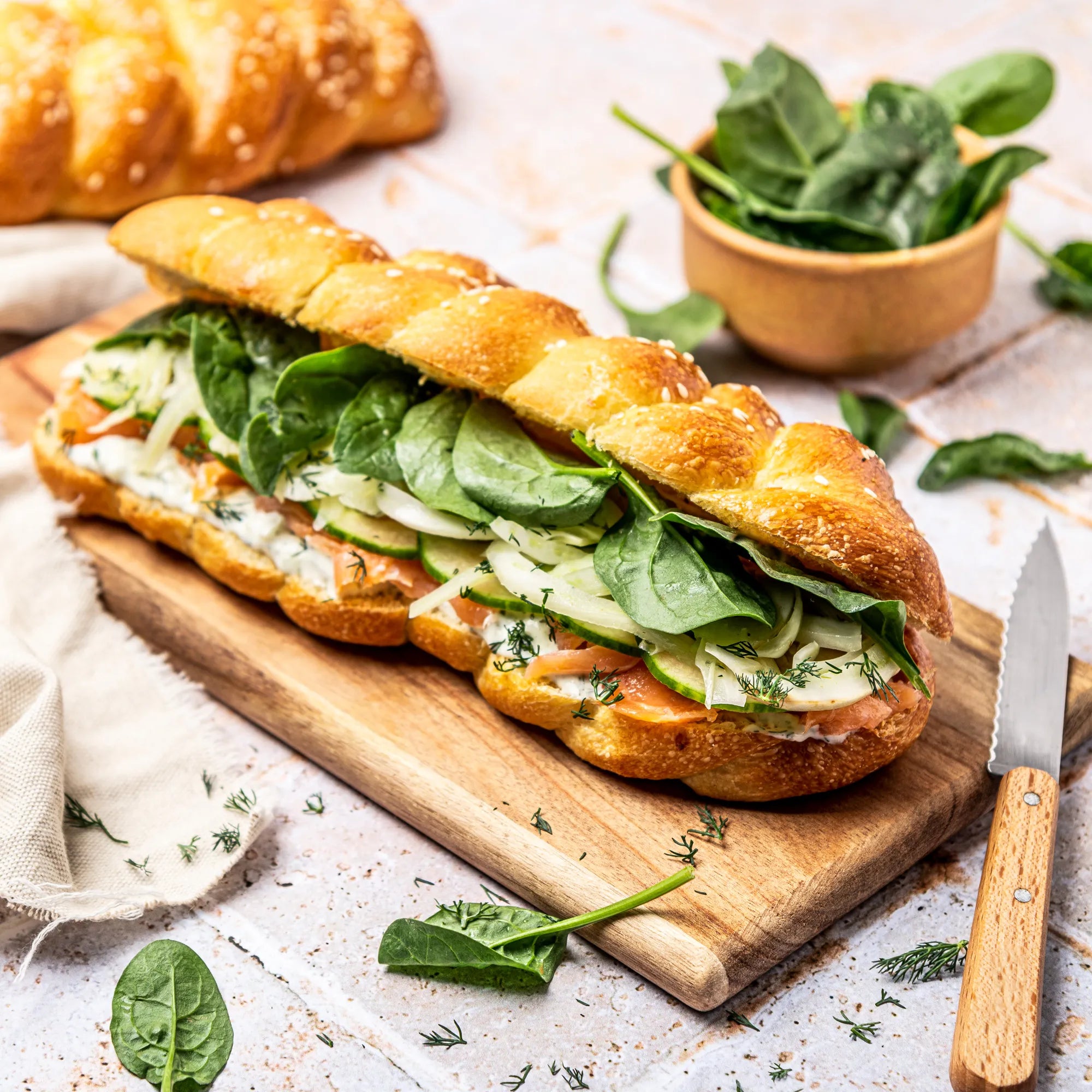 Sandwich au saumon fumé sur planche en bois : pain Hallot brioché au sésame, tzatziki de concombre, fenouil et pousses d'épinards.