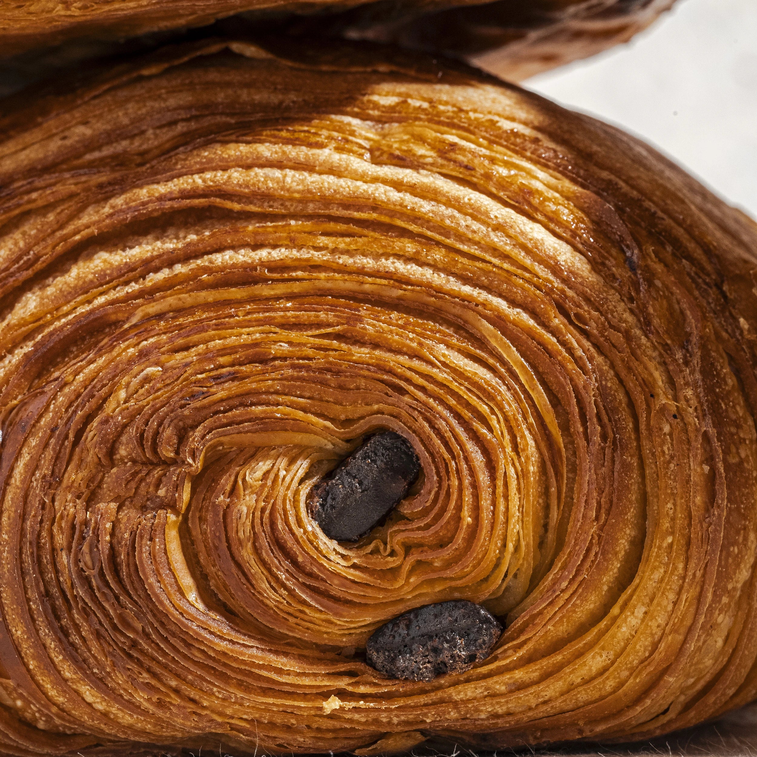 Zoom sur la spirale du feuilletage croustillant et caramélisé d'un pain au chocolat artisanal.