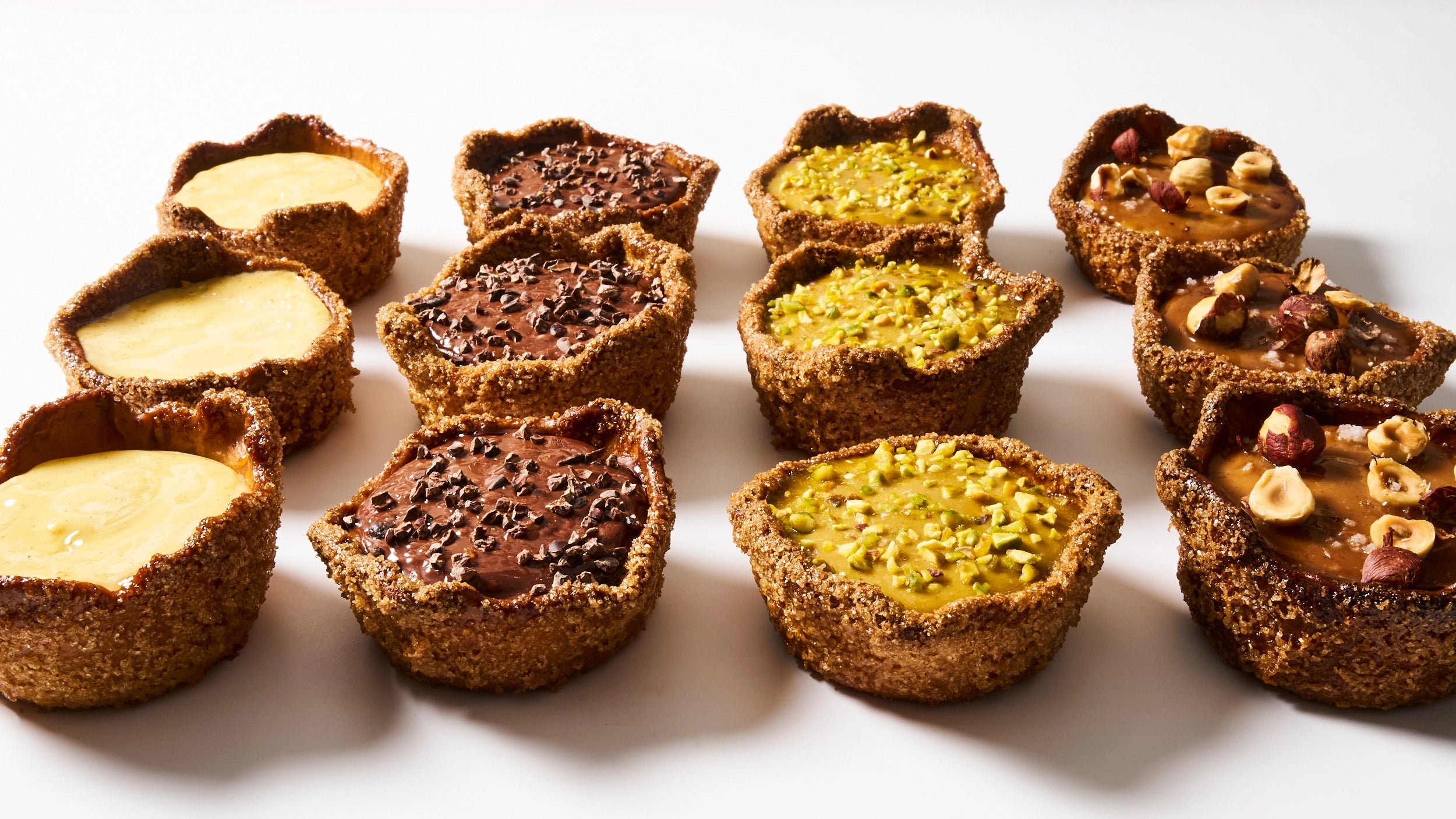 Alignement gourmand de plusieurs flans individuels signés Jeffrey Cagnes, présentant un assortiment de parfums : vanille onctueuse, chocolat intense aux éclats de cacao, pistache concassée et praliné aux noisettes et noix de pécan.