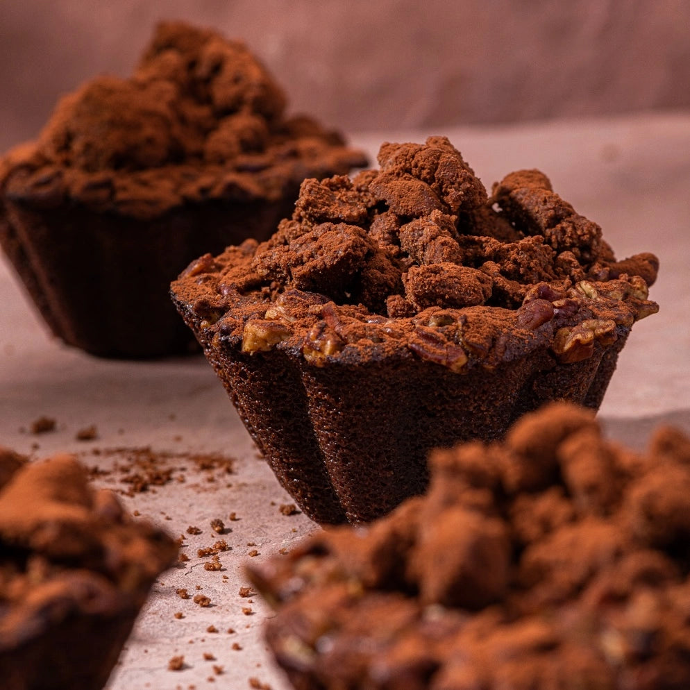 Vue en perspective de brownies individuels cuits en moules cannelés sur fond rosé.