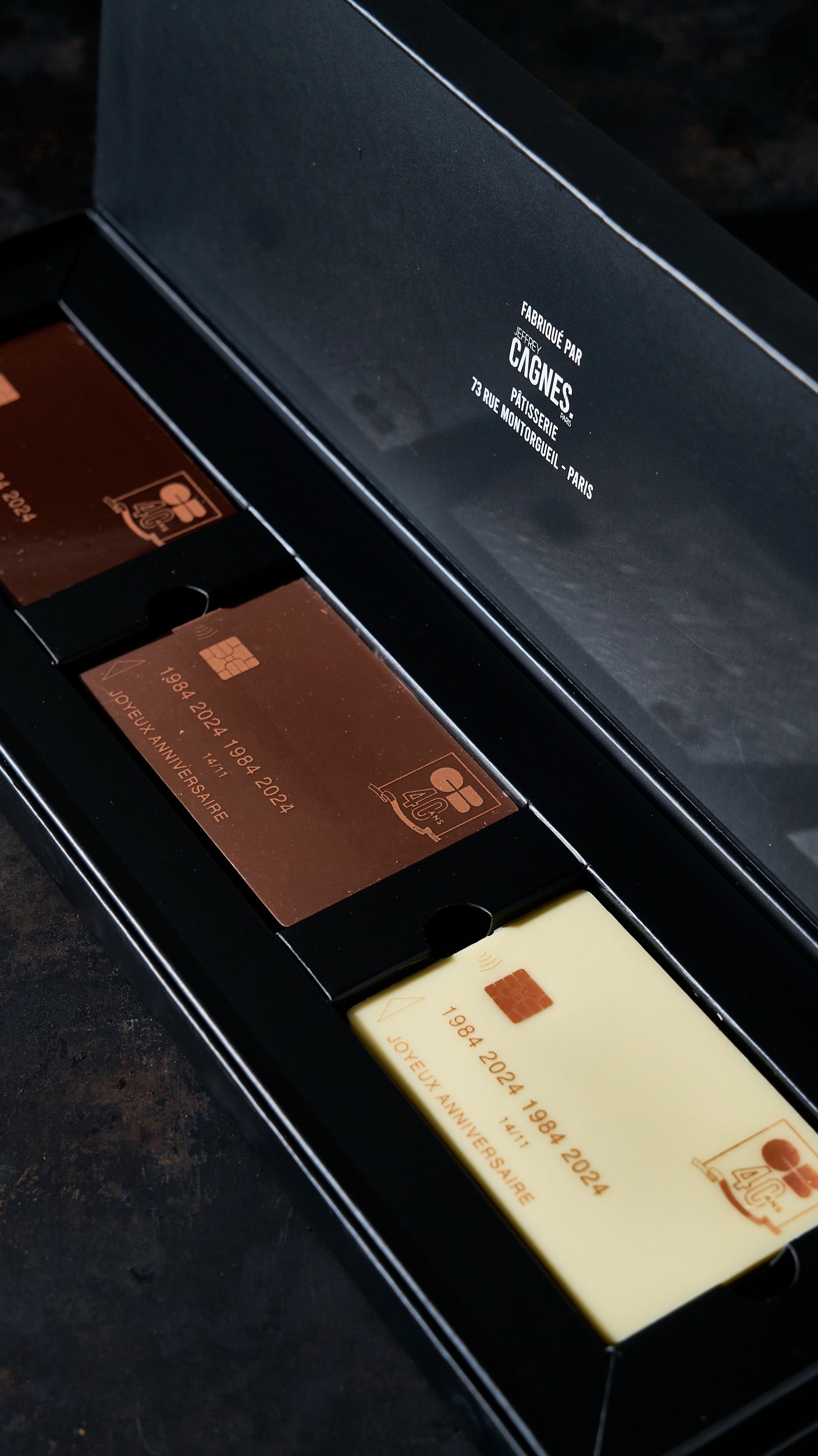 Coffret cadeau d'entreprise haut de gamme contenant des reproductions de cartes bancaires CB en chocolat noir, au lait et blanc, personnalisé pour l'anniversaire de la société Cartes Bancaires par Jeffrey Cagnes.