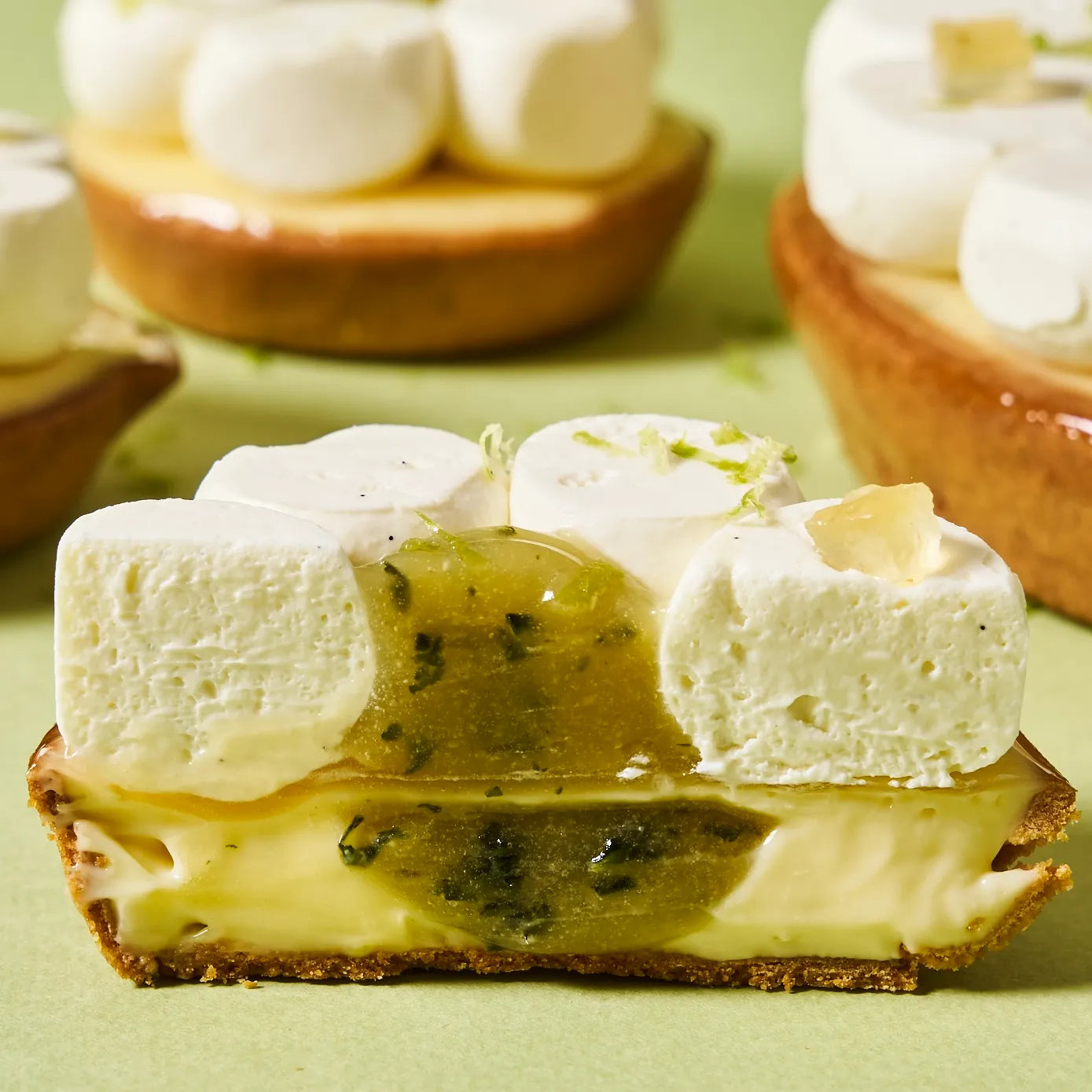Coupe transversale d'une part de tarte au citron vert montrant la pâte sucrée croustillante, le crémeux onctueux et le cœur de confit au basilic.