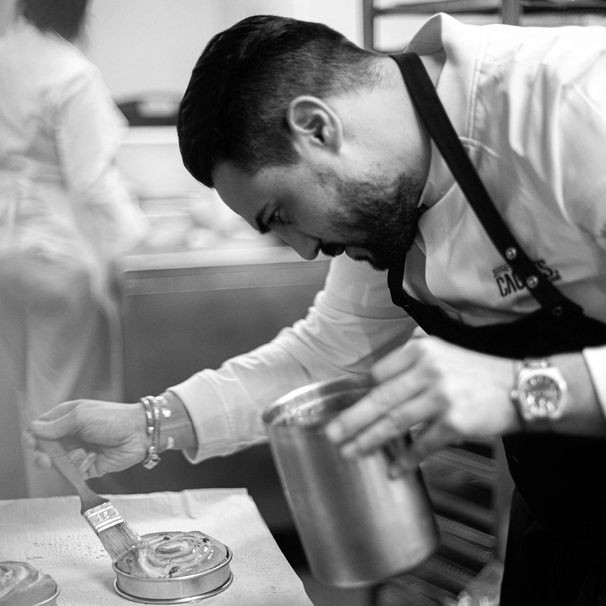 Jeffrey Cagnes appliquant de la dorure au pinceau sur des pâtisseries individuelles dans son laboratoire, avec un tablier noir.