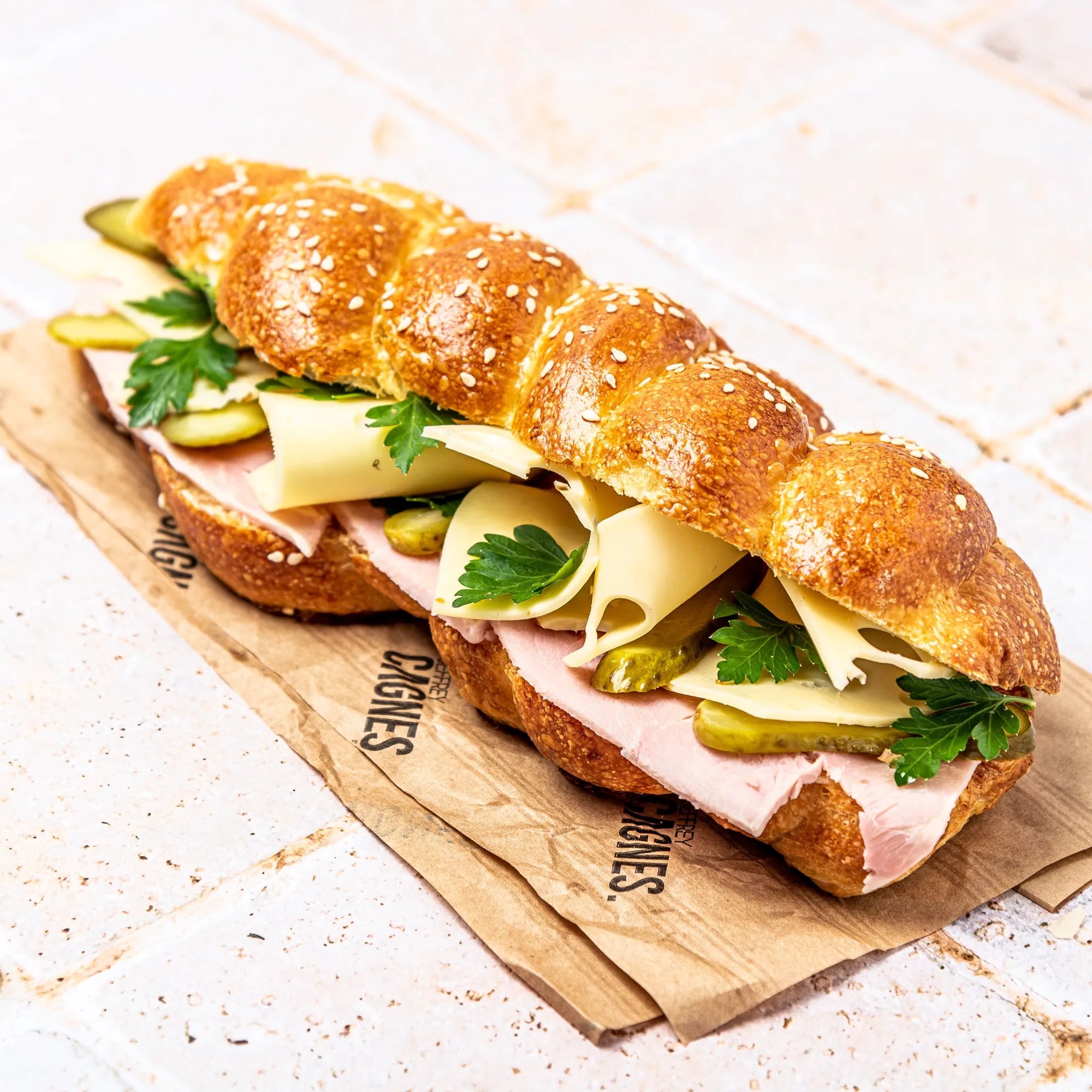 Vue d'ensemble du sandwich Le Parisien de Jeffrey Cagnes reposant sur son papier kraft siglé.