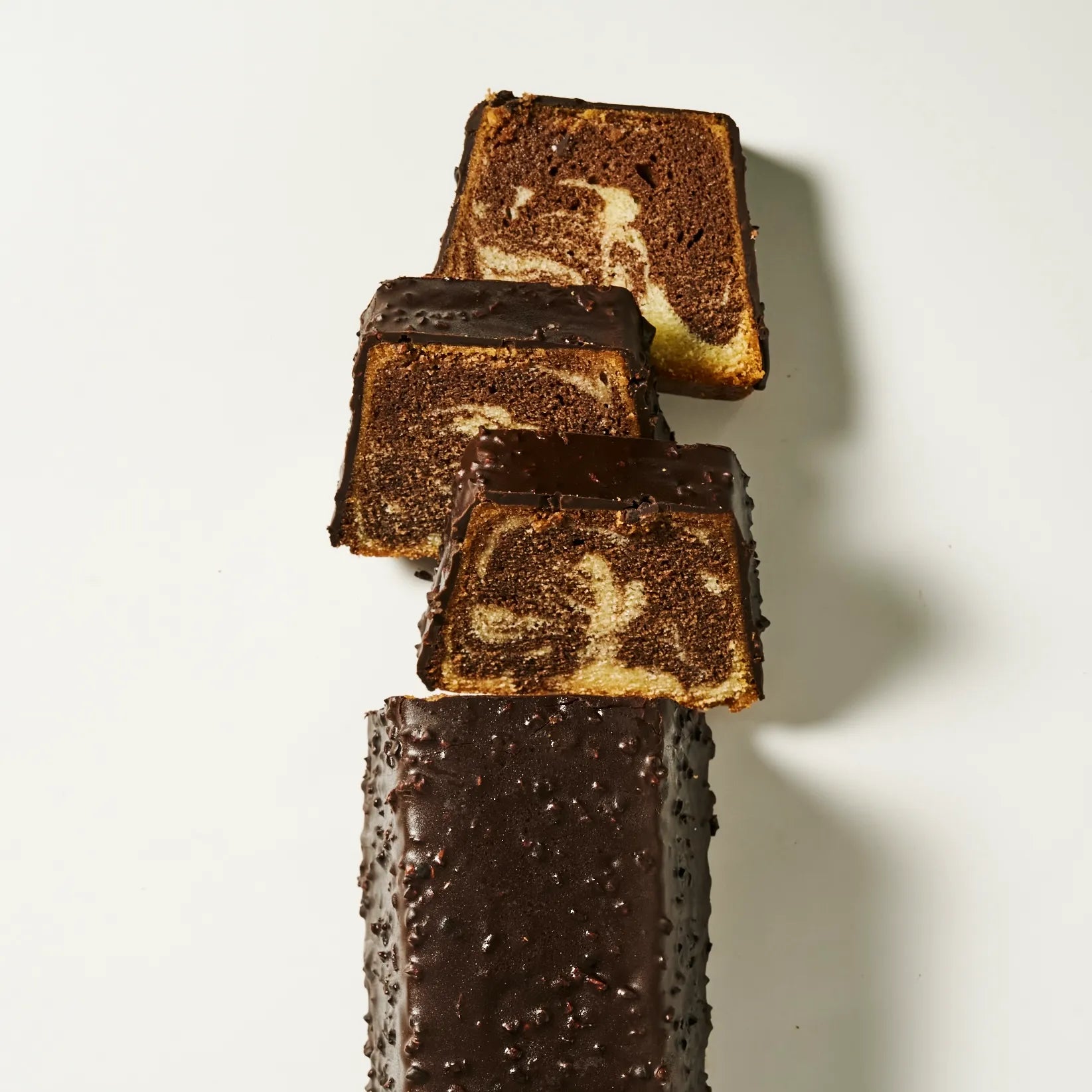 Alignement de parts de cake marbré vanille et chocolat de Jeffrey Cagnes recouvertes d'un enrobage chocolat noir et éclats d'amandes.