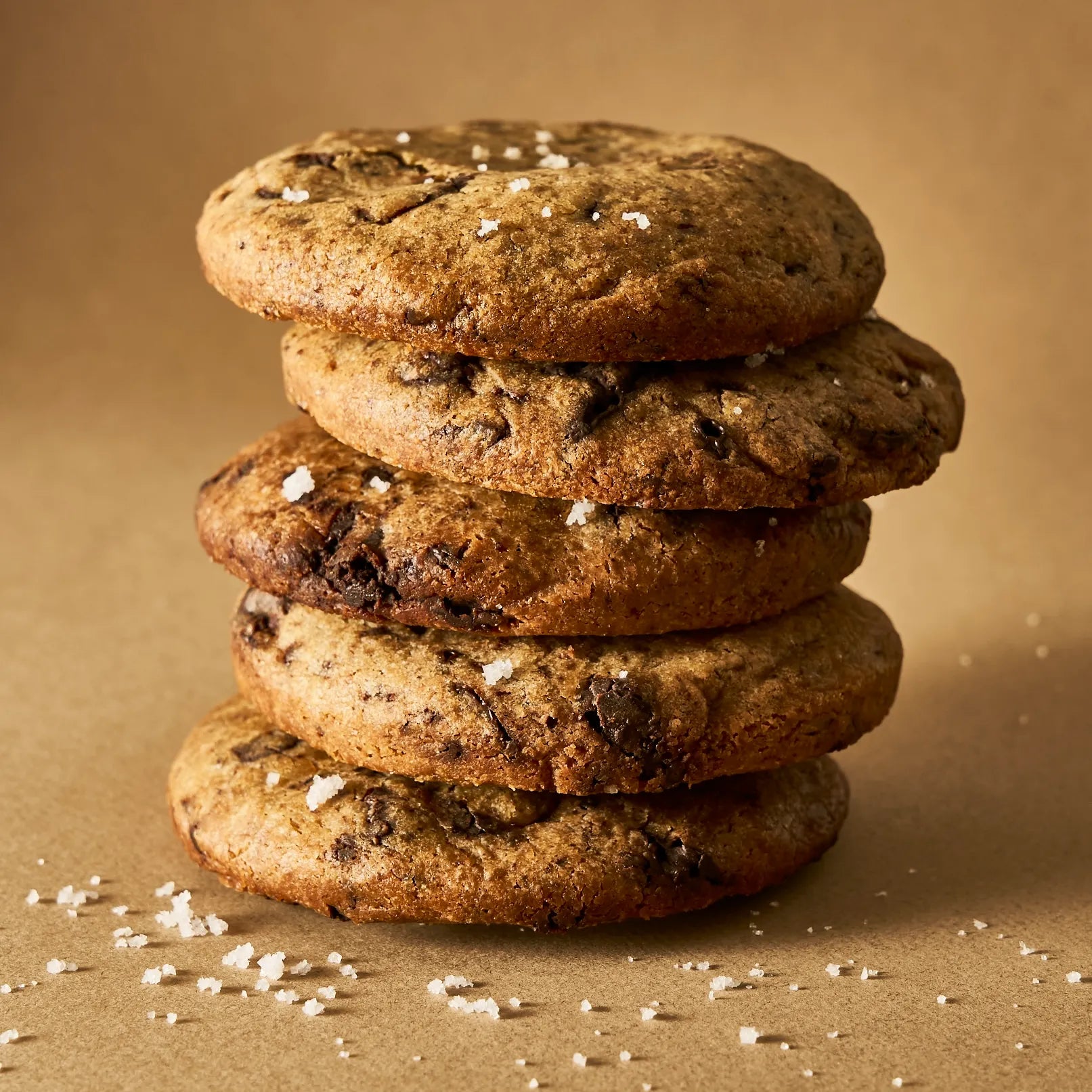 Pile de cookies artisanaux au chocolat noir parsemés de gros cristaux de fleur de sel, illustrant une cuisson dorée parfaite.