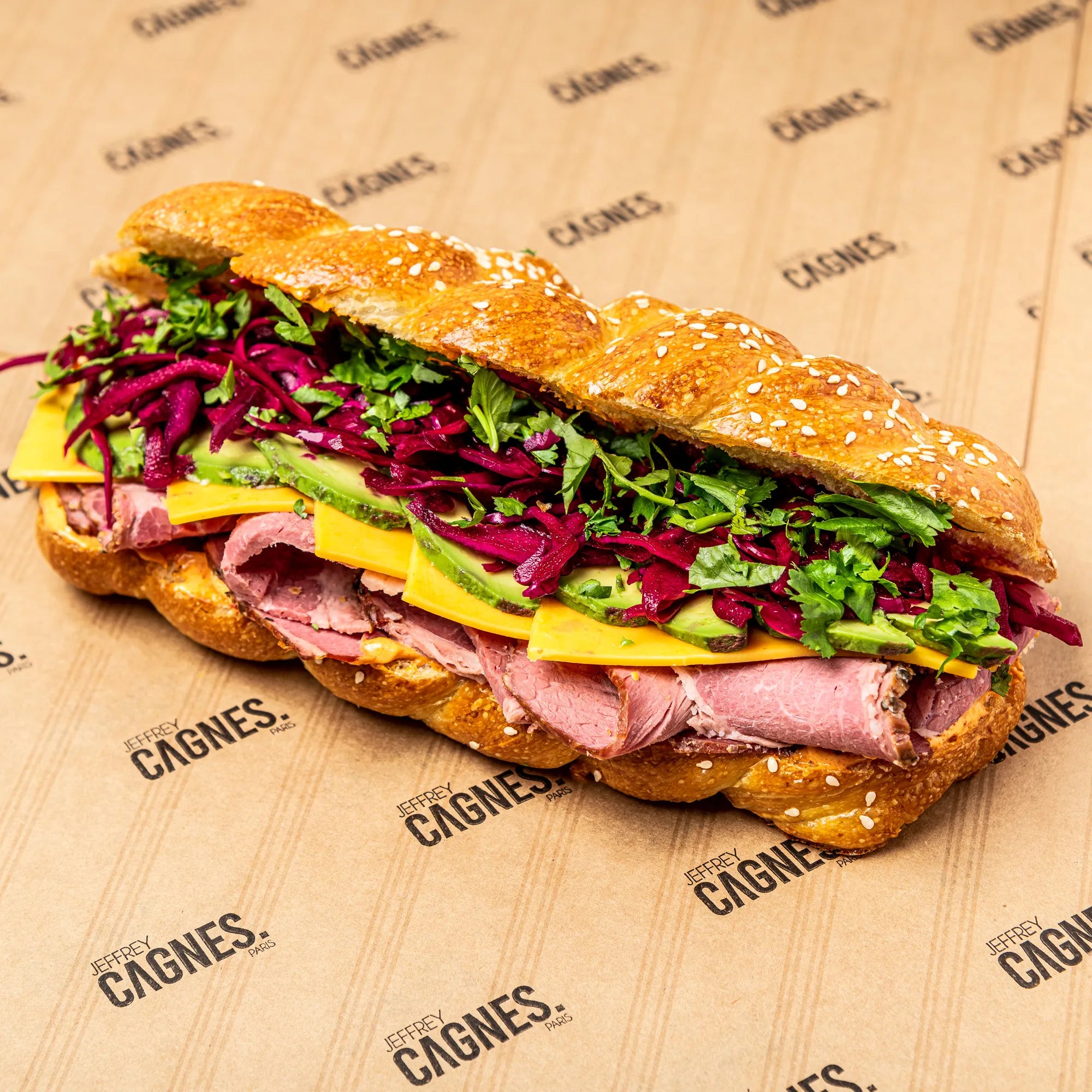 Sandwich Pastrami complet sur papier Jeffrey Cagnes : pain Hallot brioché tressé au sésame, pastrami de bœuf, cheddar et chou rouge.