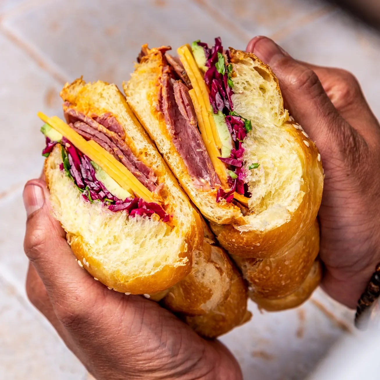 Coupe transversale d'un sandwich Pastrami dévoilant la mie aérée du pain Hallot, les tranches de pastrami et le cheddar.