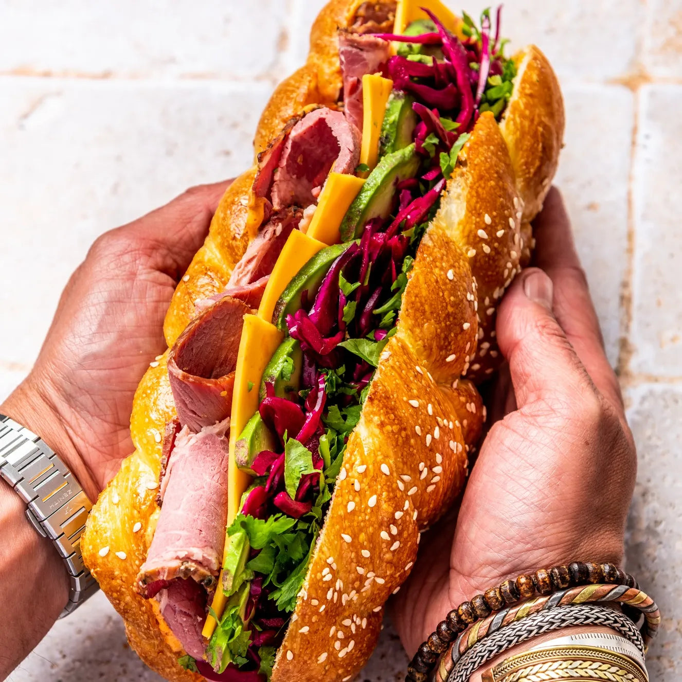 Prise en main d'un généreux sandwich Pastrami montrant la garniture colorée et le pain Hallot moelleux.