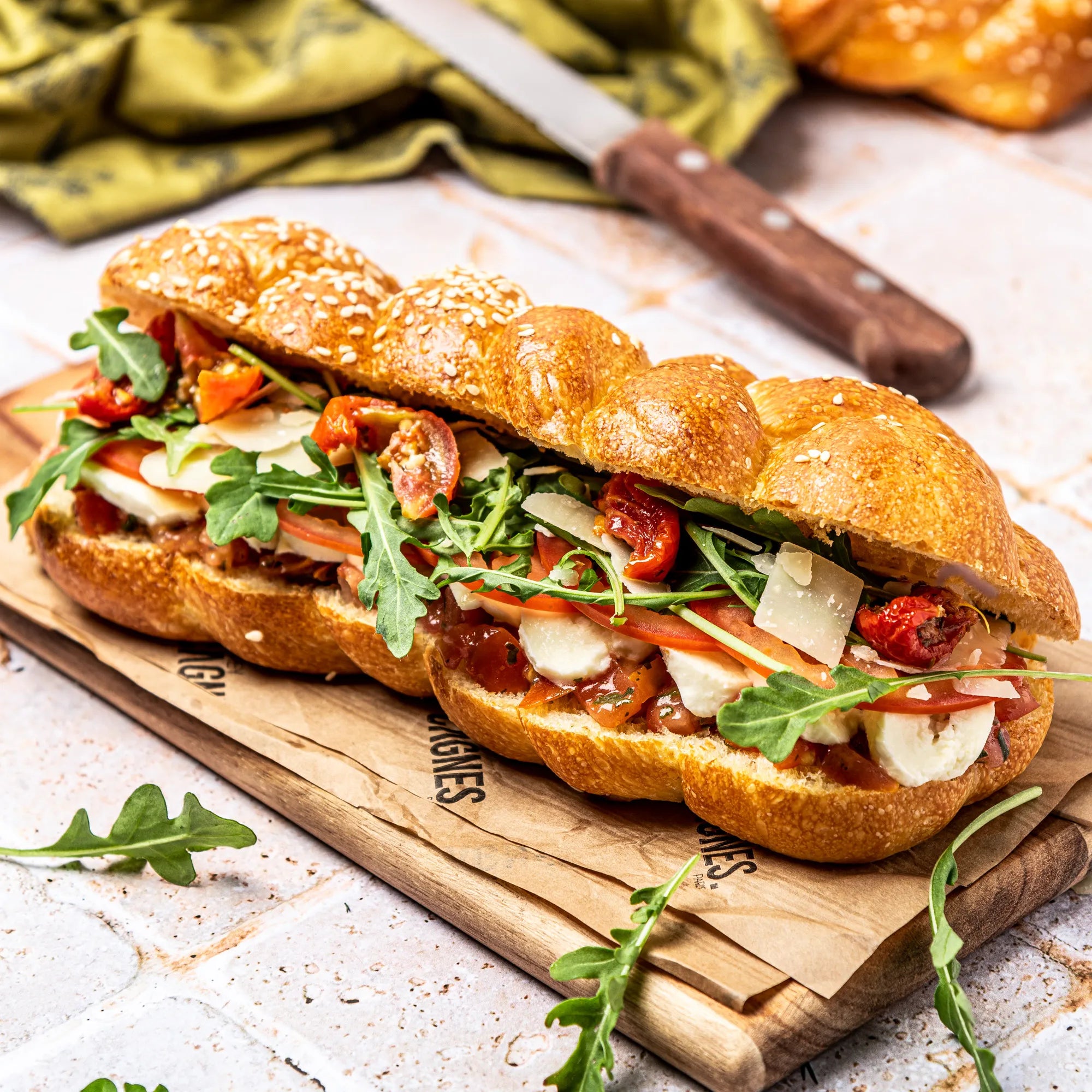 Sandwich Veggie garni sur planche de bois : pain Hallot brioché tressé, mozzarella, tomates fraîches, roquette et copeaux de parmesan.