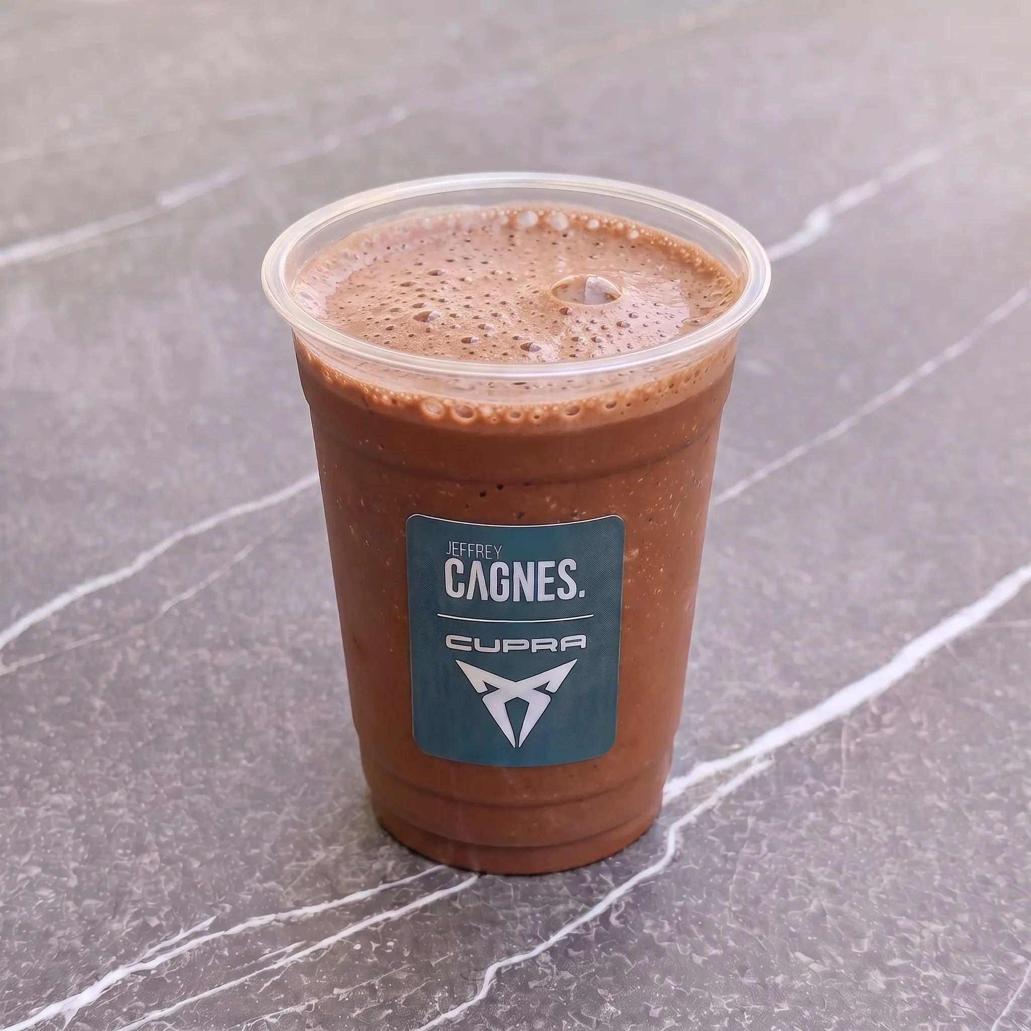 Gobelet transparent de smoothie Banane Nocciolata par Jeffrey Cagnes x Cupra, montrant une texture onctueuse au cacao, noisette et fleur de sel.