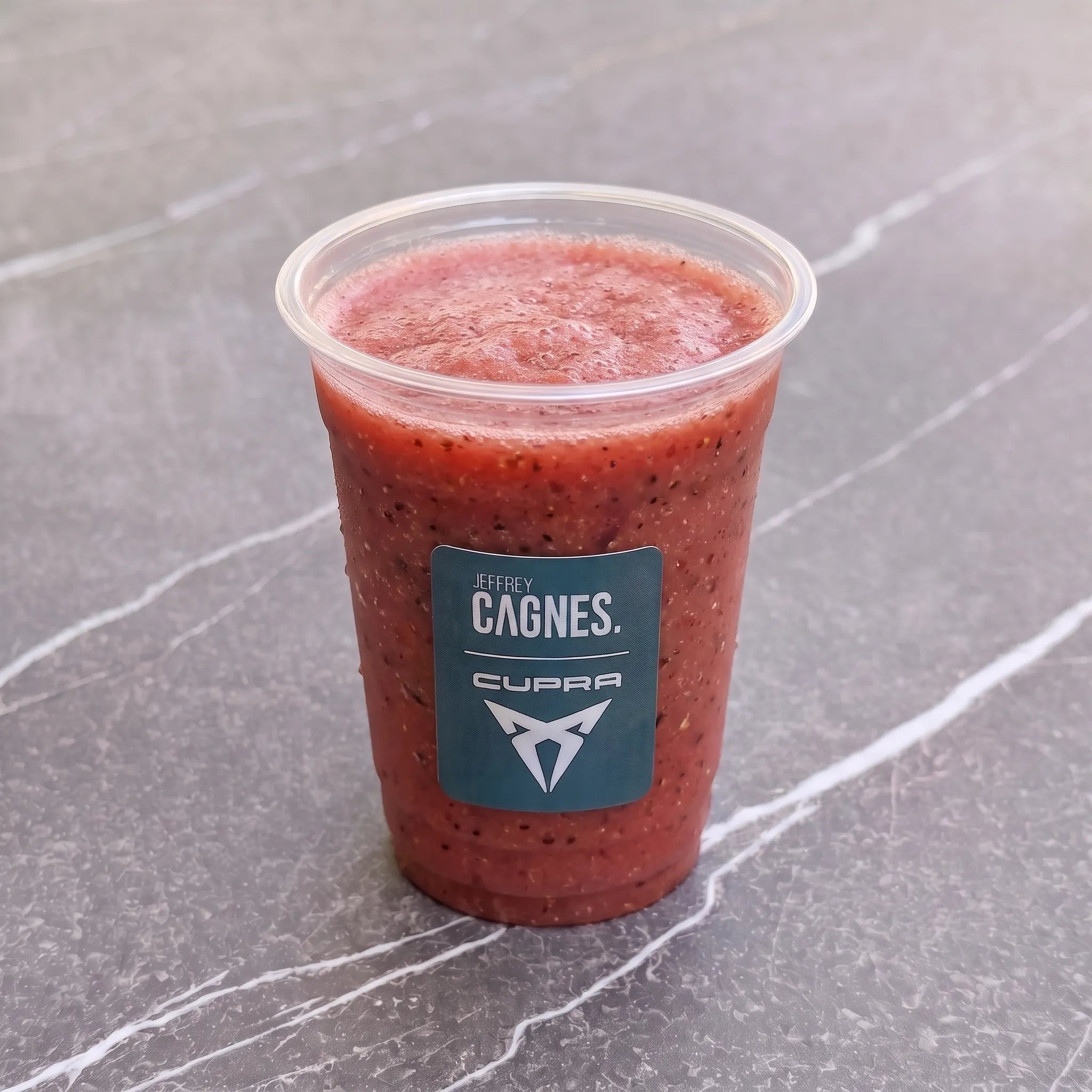 Gobelet transparent de smoothie Rubis Menthe signé Jeffrey Cagnes x Cupra, révélant une boisson fraise pastèque menthe à la couleur rouge rubis intense.
