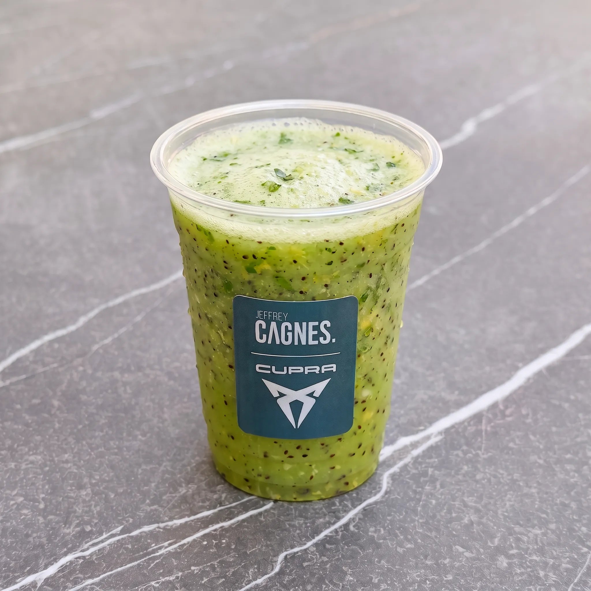 Gobelet transparent de smoothie Signature vert vif signé Jeffrey Cagnes x Cupra, à base de kiwi, citron et éclats de basilic frais.