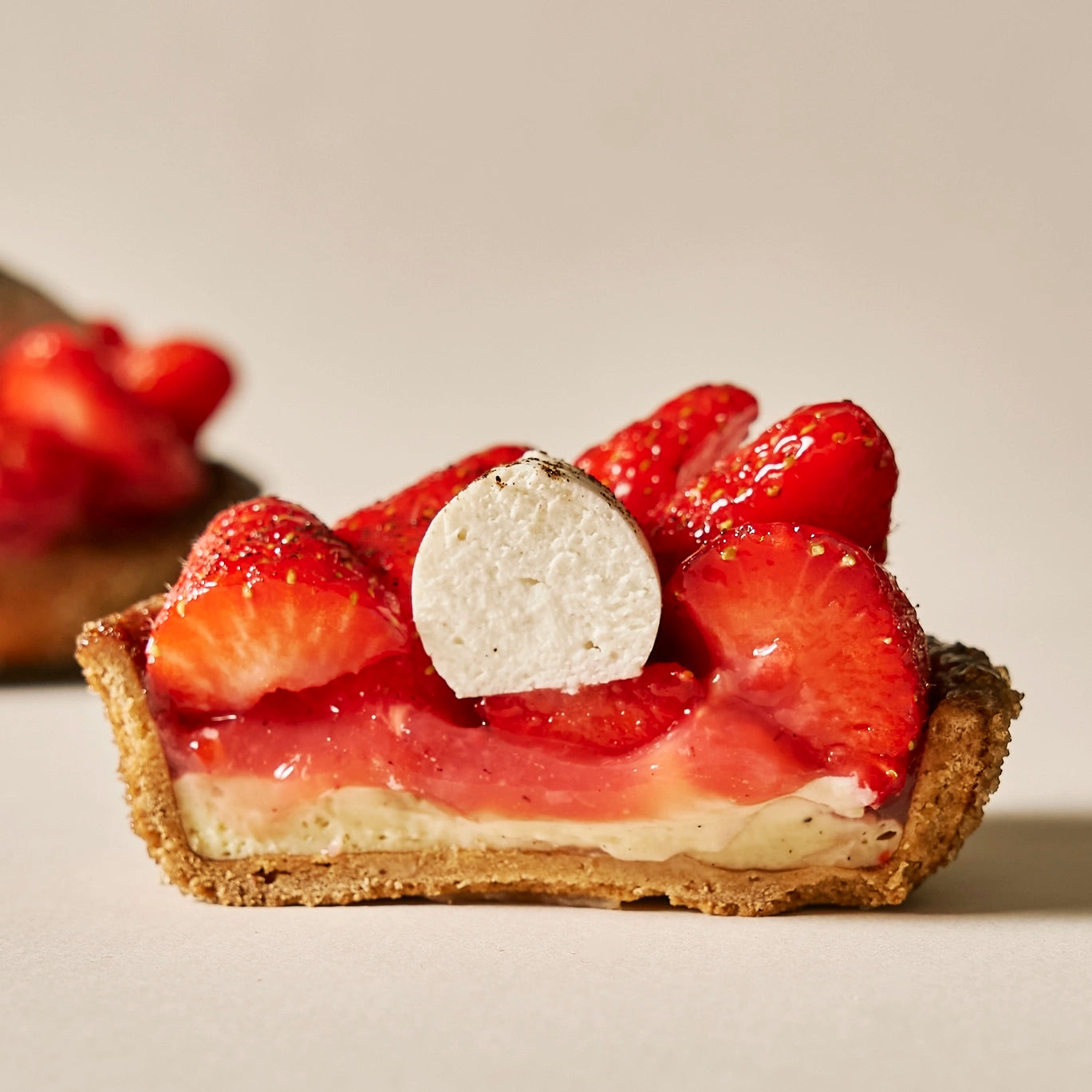 Coupe transversale d'une tarte aux fraises montrant la pâte sucrée, le crémeux vanille, le confit de fraises et la chantilly mascarpone.