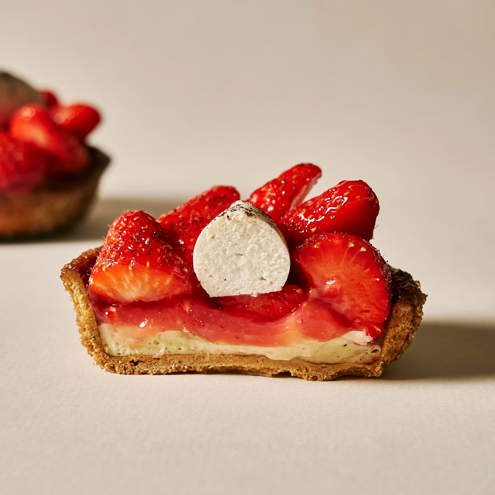 Détail en gros plan de la coupe d'une tartelette aux fraises dévoilant le cœur garni et la chantilly vanille mascarpone.
