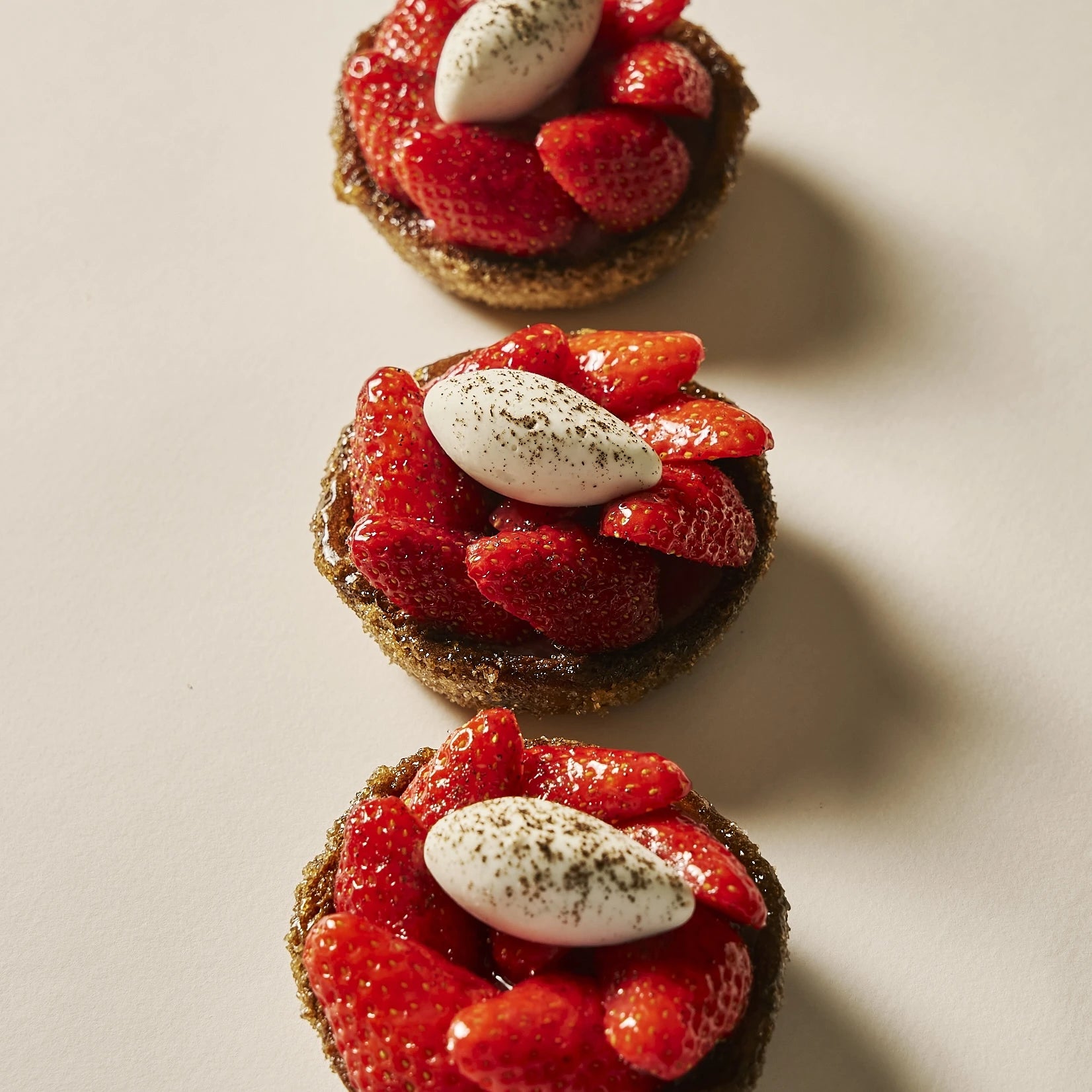 Trois tartes aux fraises individuelles alignées, garnies de fraises fraîches brillantes et de quenelles de chantilly vanille mascarpone.