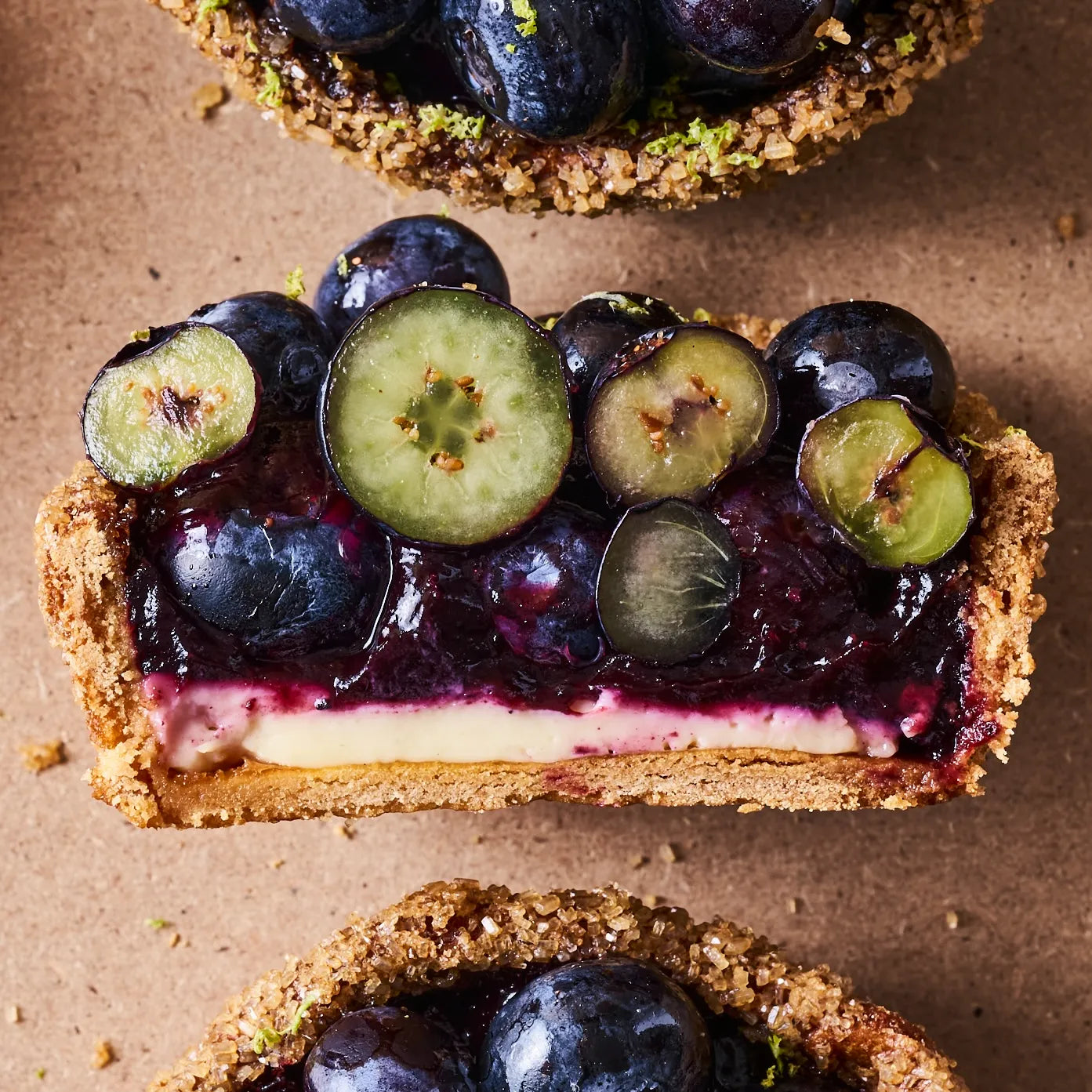 Gros plan sur la coupe nette d'une tartelette aux myrtilles montrant l'équilibre des couches de vanille et de confit.