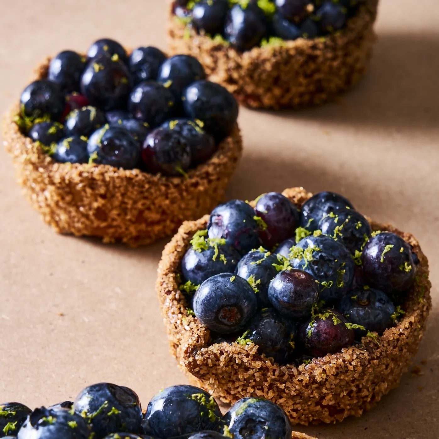 Trois tartelettes individuelles aux myrtilles fraîches disposées en perspective.