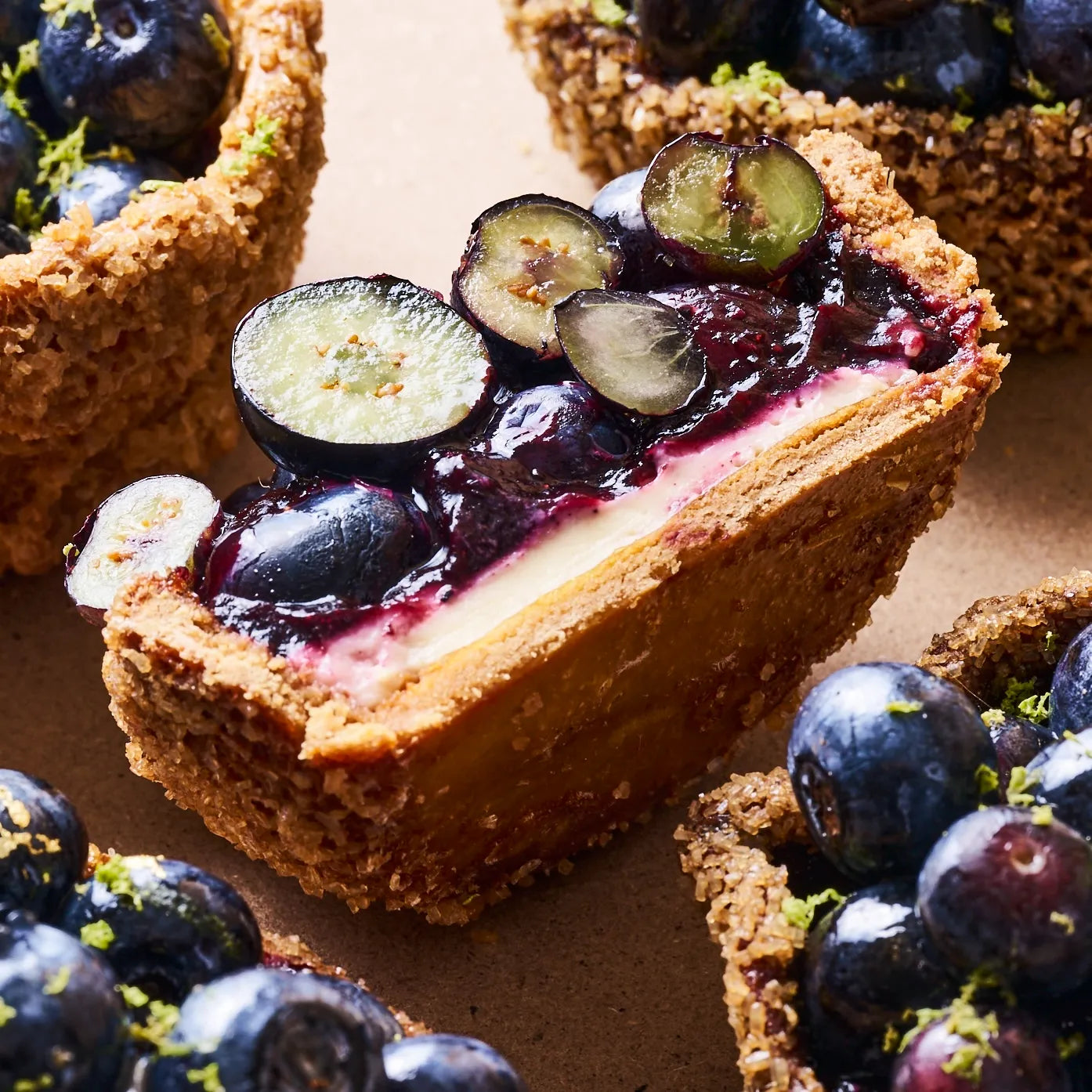 Vue en perspective de la tranche d'une tartelette aux myrtilles mettant en valeur la texture du biscuit et du crémeux.