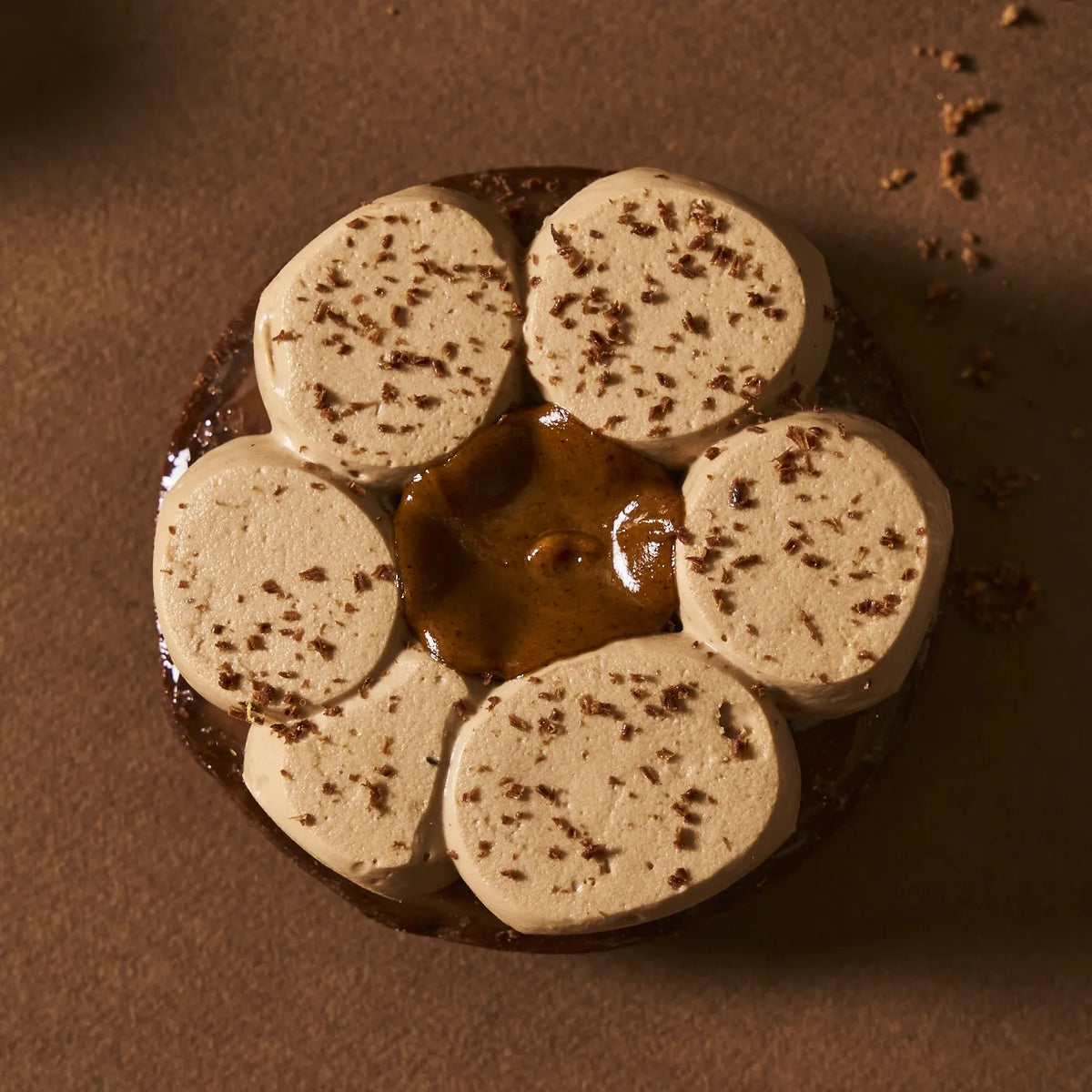 Gros plan sur le pochage de la crème namelaka au chocolat au lait et fève de tonka, saupoudré de copeaux de cacao.