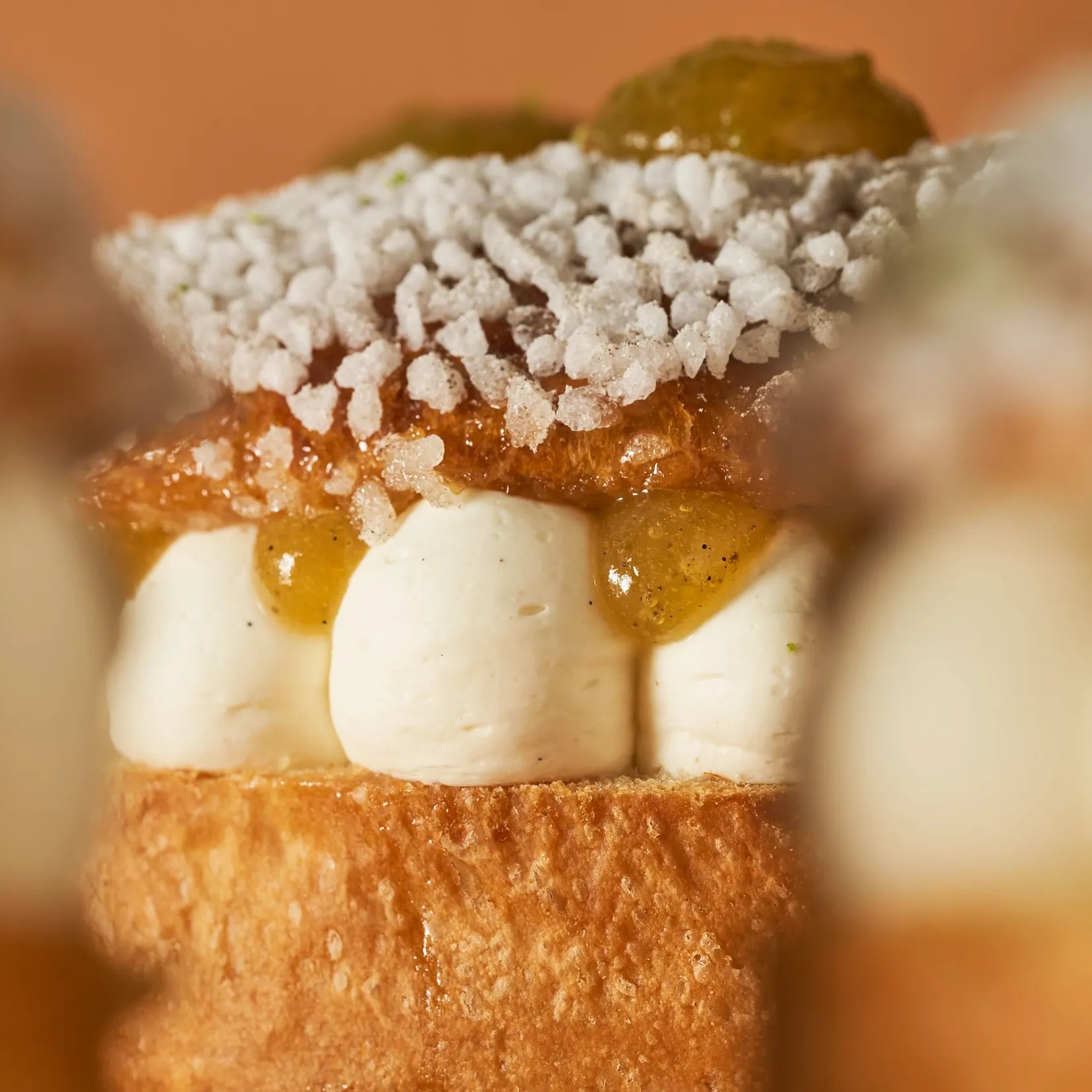 Gros plan latéral sur la texture onctueuse de la crème montée fleur d'oranger et les grains de sucre de la Tarte Tropézienne.
