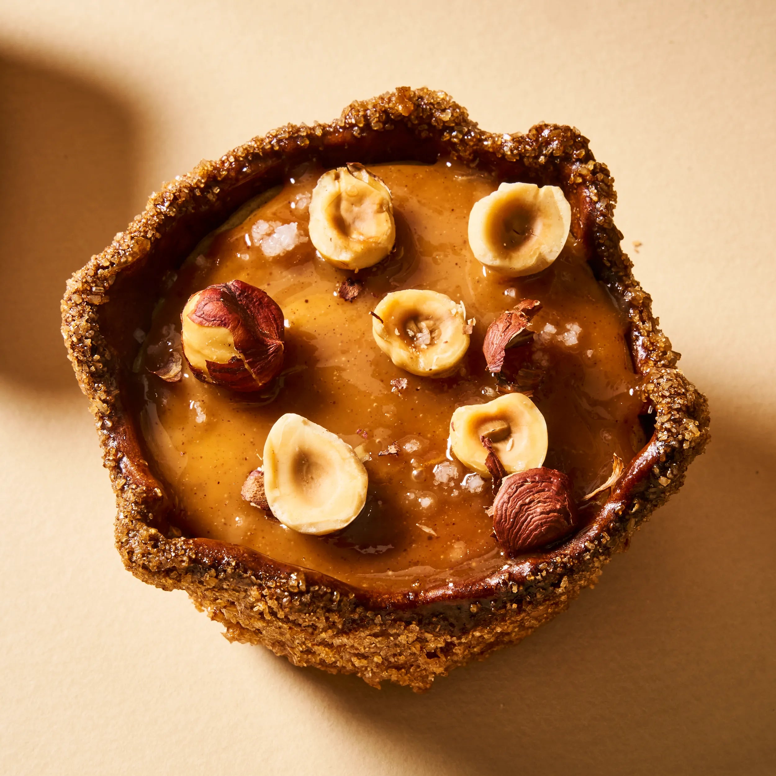 Gros plan sur le dessus d'un flan noisette, montrant les éclats de fleur de sel et les noisettes entières disposées sur un praliné maison coulant.