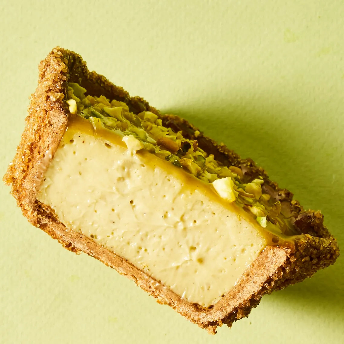 Gros plan incliné sur une demi-part de flan pistache, soulignant le contraste parfait entre le croûtage caramélisé à la cassonade et le cœur ultra-onctueux.